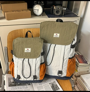 Two color-block nylon backpacks with contrast olive and grey panels on a wooden chair