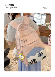 Detail of pink student backpack featuring blue cartoon house embroidery and dual cute charms