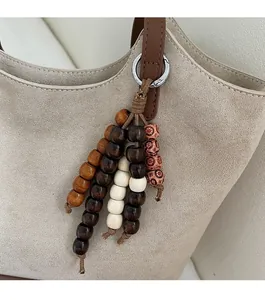 Detailed close-up of a bohemian wooden bead tassel pendant on a beige suede tote bag