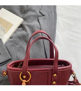 Detailaufnahme der burgunderroten Handtasche mit goldenen Beschlägen und Tragegriffen