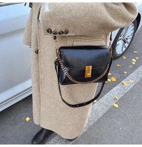 Détail du petit sac bandoulière vintage noir avec chaîne dorée et boucle sur manteau laine