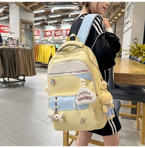 Detail of yellow nylon backpack with multi-pocket design and cute cartoon charms