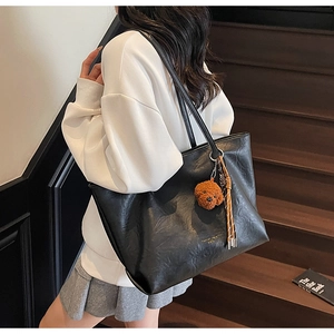 Detail of black PU leather tote bag with brown bear charm and woven tassel detail