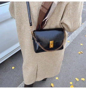 Détail d'un sac à rabat en cuir noir brillant avec fermoir doré sur fond de manteau kaki