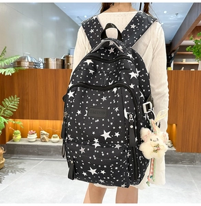 Side view of black star pattern backpack with multiple pockets and plush pendant