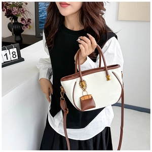 Detail of elegant two-tone leather tote bag featuring brown straps and a mini charm