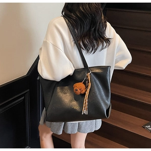 Detail of black large tote bag with gold lettering, teddy bear charm, and woven tassel