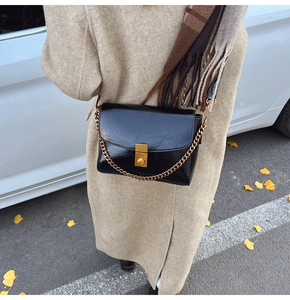 Détail d'un sac bandoulière noir brillant avec fermoir doré porté sur un manteau camel