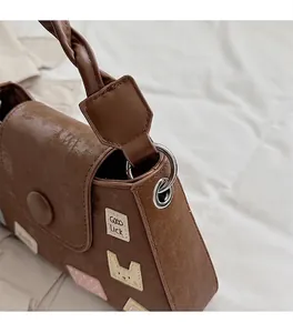 Detalle del bolso tipo cubo de cuero sintético marrón con hebillas plateadas y asa trenzada