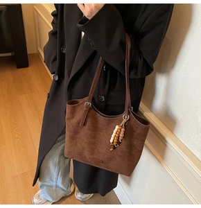 Detail of coffee brown suede tote bag with leather straps and boho beaded keychain accessory