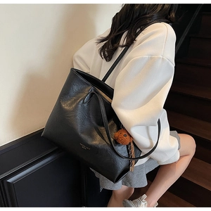 Detail of large black leather tote bag with gold lettering and brown plush bear charm