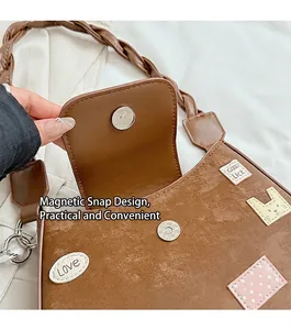 Detalle del cierre magnético y parches decorativos en un bolso de cuero de color marrón