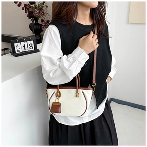 Detail of white tote bag with brown leather trim and mini purse charm on adjustable strap