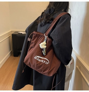Detail der dunkelbraunen Nylon-Tote-Tasche mit BANATU-Logo und gelbem Plüsch-Mondanhänger