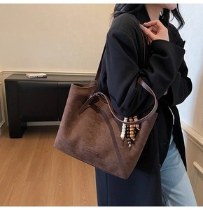 Detailed close-up of brown suede tote bag with brand logo and colorful beaded charm