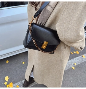Sac bandoulière noir classique avec boucle dorée porté par un mannequin en automne
