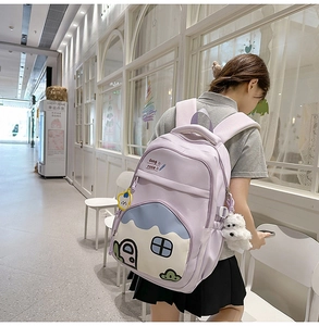 Detail of light purple school backpack with cartoon house decor and plush puppy charm