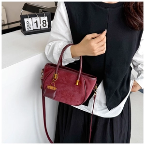 Detail of burgundy suede bucket bag with round handles and chic metal chain pendant