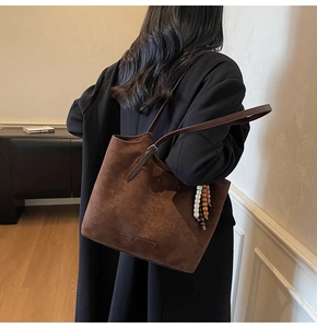 Detail of dark brown suede tote bag featuring a beaded charm and slim leather straps