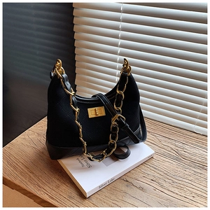 Detailed view of black quilted faux leather bag with golden chain and clasp on wood