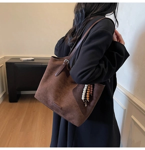 Detail of dark brown suede tote bag with ethnic beaded charm and leather logo tag