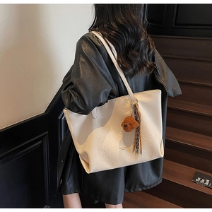 Detail of cream tote bag with bear charm on model in minimalist setting