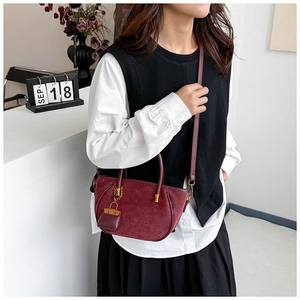 Detail of burgundy suede bucket bag featuring cylindrical handle and gold charm