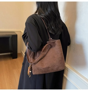 Detail of a brown faux suede tote bag with colorful beaded charm on a black coat