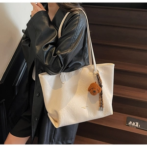 Detail view of cream tote bag with wrinkled texture, teddy bear charm, and woven tassel
