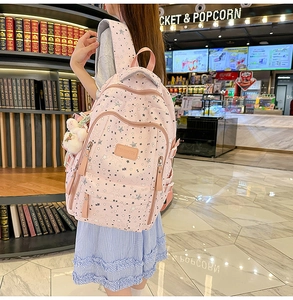 Pink waterproof backpack with star print and plush pendant worn by model in a library