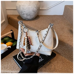 Detail of white woven crossbody bag with chunky silver chain on design books
