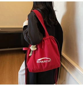 Detailansicht einer großen roten Segeltuch-Tasche mit Kordelzug und grünem Plüsch-Anhänger