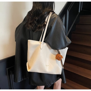 Detail of white pleated tote bag with golden logo and cute brown teddy bear charm