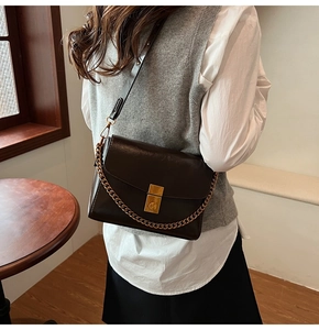 Détail d'un sac à rabat marron vintage avec fermoir doré et chaîne en métal décorative