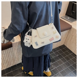 Primer plano de un bolso bucket de cuero blanco con parches de dibujos y un colgante de perro