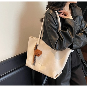 Close-up of beige faux leather tote bag with a brown teddy bear and tassel charm