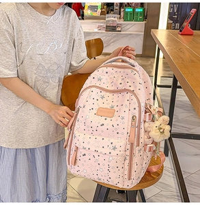 Side view of a pink backpack with star prints and a plush bear pendant accessory