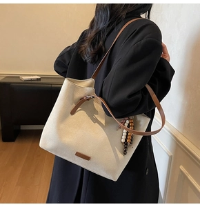 Close-up of cream suede tote bag featuring brown leather straps and vintage beaded tassel