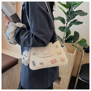 Detalle de un bolso blanco con parches de dibujos animados y un dije de perro de felpa