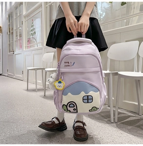 Detail of lavender school backpack featuring a cartoon house pocket and plush charms