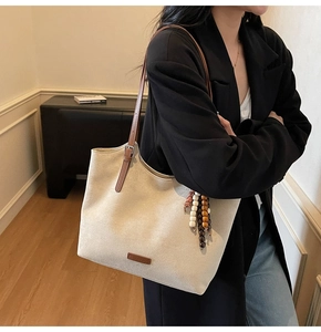 Detail of cream suede tote bag featuring brown leather straps and boho beaded charm