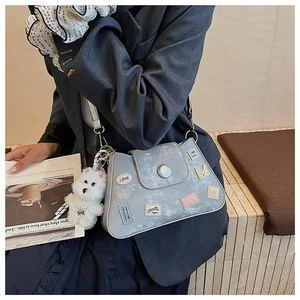 Detalle de bolso gris de hombro con parches de dibujos y colgante de perrito peluche