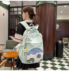 Detail of mint green school backpack with cartoon house print and plush pendant