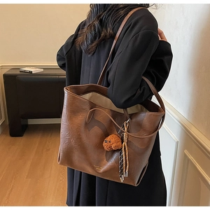 Detail of large brown PU leather tote bag with teddy bear pendant and striped ribbon