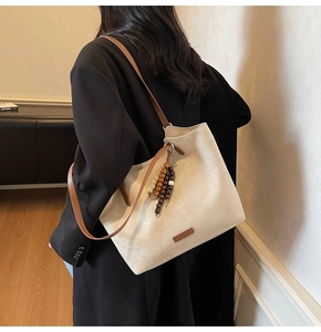 Detail of off-white suede tote bag with brown leather strap and wooden bead tassel