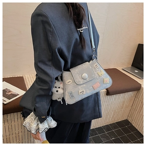 Detalle del bolso tipo cubo gris con bordados y un tierno colgante de peluche blanco