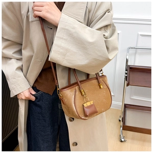 Detail of camel suede shoulder bag with mini Kelly charm on neutral trench coat