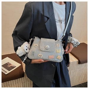 Detalle de bolso cubo azul metalizado con parches y un colgante de peluche de perrito