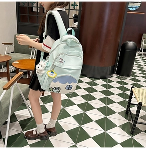 Detail of mint green school backpack with cartoon house pocket and plush dog charm