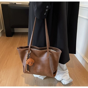 Detailed texture of brown faux leather tote bag with a cute teddy bear charm hanging